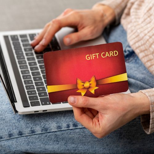 A Woman Holding Up a Visa Gift Card Debit While Using a Laptop