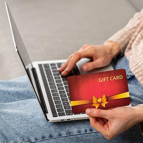 A Woman Using a Laptop and Displaying a Visa Online Gift Card to the Camera.