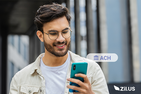 ACH Payment on Mobile – a Young Man Smiling While Using His Smartphone Outdoors, Representing Easy and Secure ACH Transactions.